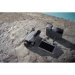 Compact drone with remote control and rechargeable batteries on rocky terrain for aerial photography.