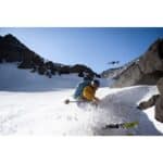 High-altitude skier with drone capturing snow sports adventure on mountain slope.